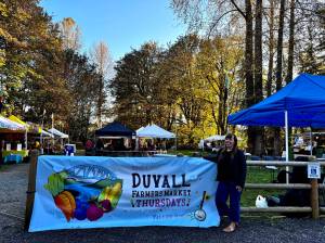 Duvall Farmers Market Board president Alex Yearout stands with the markets new banner on Oct. 3, 2024. (Grace Gorenflo/Valley Record)