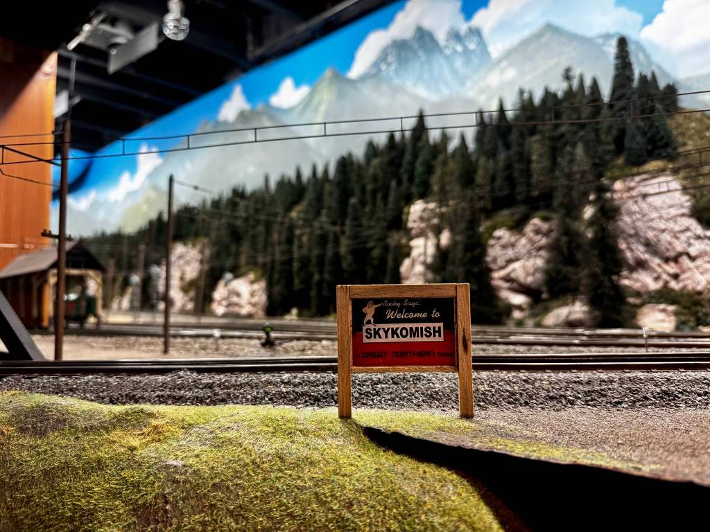 A miniature replica of the Welcome to Skykomish sign sits with a backdrop of handmade trees and painted clouds. (Grace Gorenflo/Valley Record)