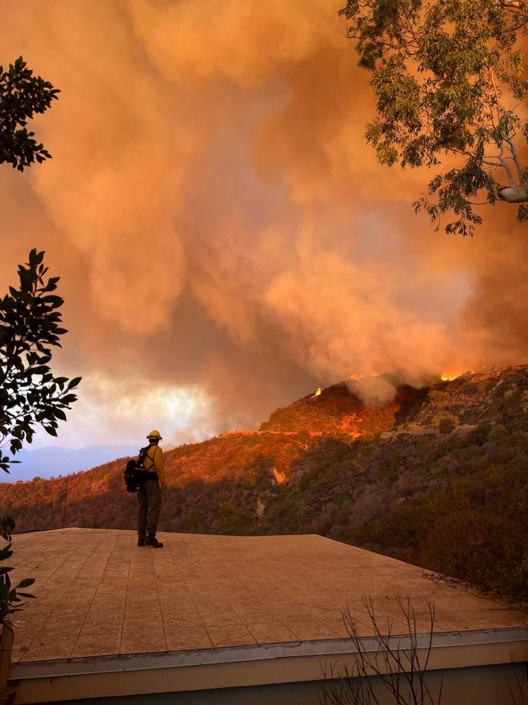 A firefighter stands against a backdrop of wildfire in California. Photo courtesy of the Fall City Fire Department