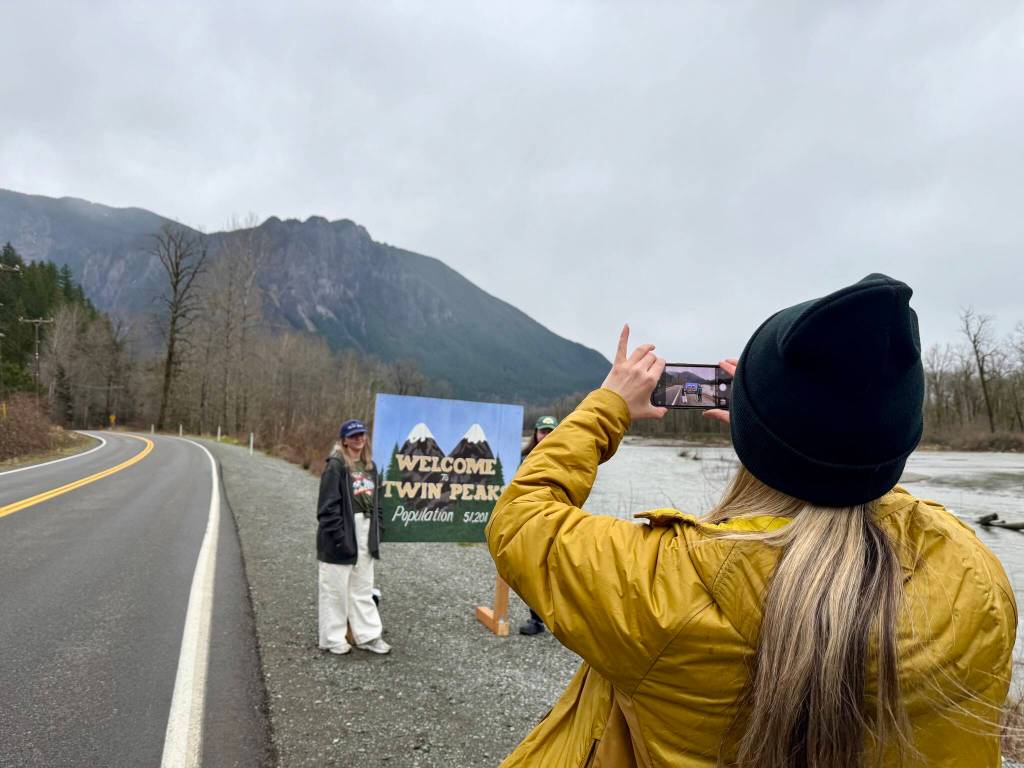 Jessica Self, executive director of the North Bend Downtown Foundation, snaps a photo of fans posing with the Welcome to Twin Peaks sign, Feb. 24, 2025.