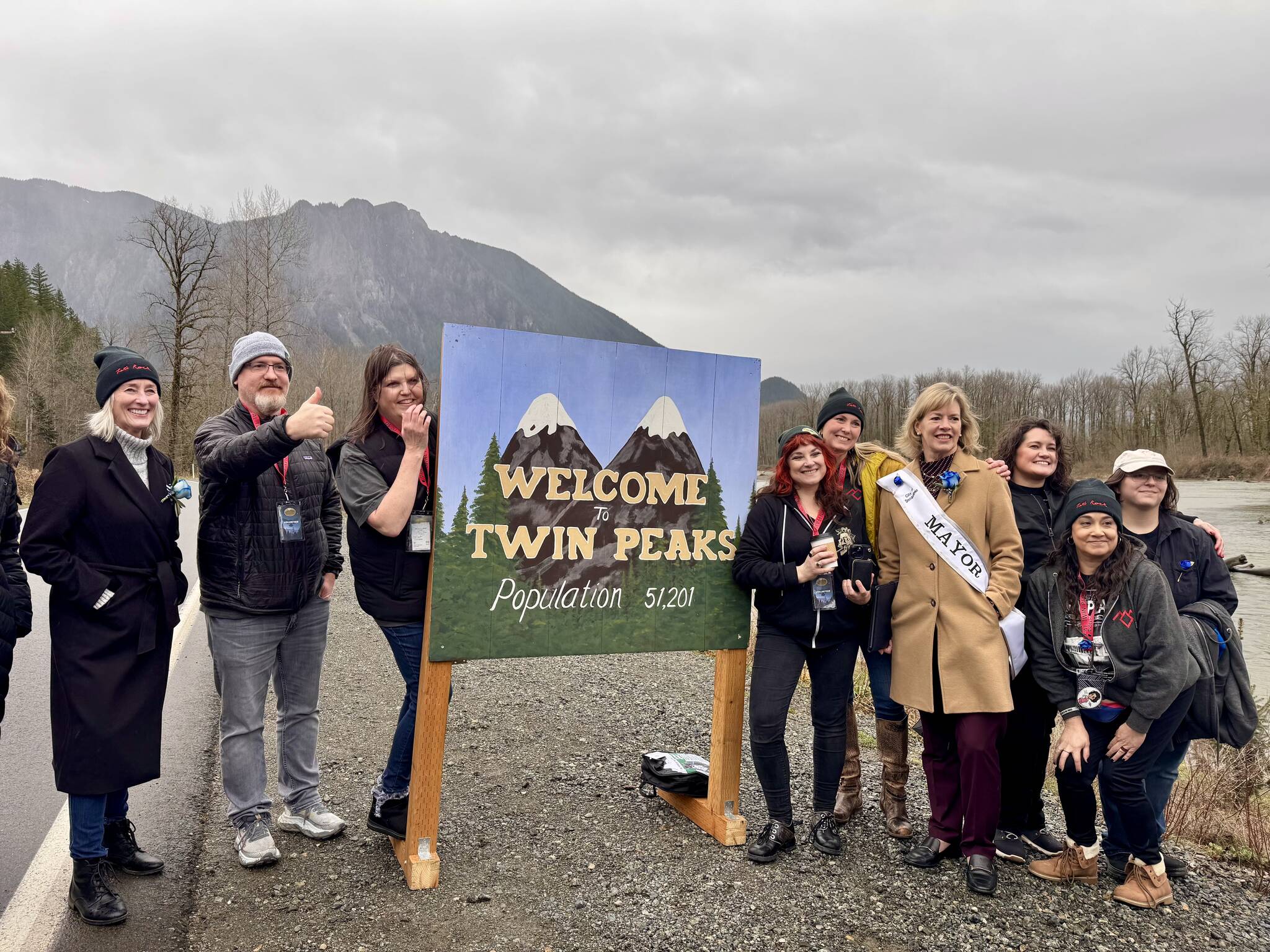 Government officials and members of Real Twin Peaks stand for a photo with the Welcome to Twin Peaks sign, Feb. 25, 2025.