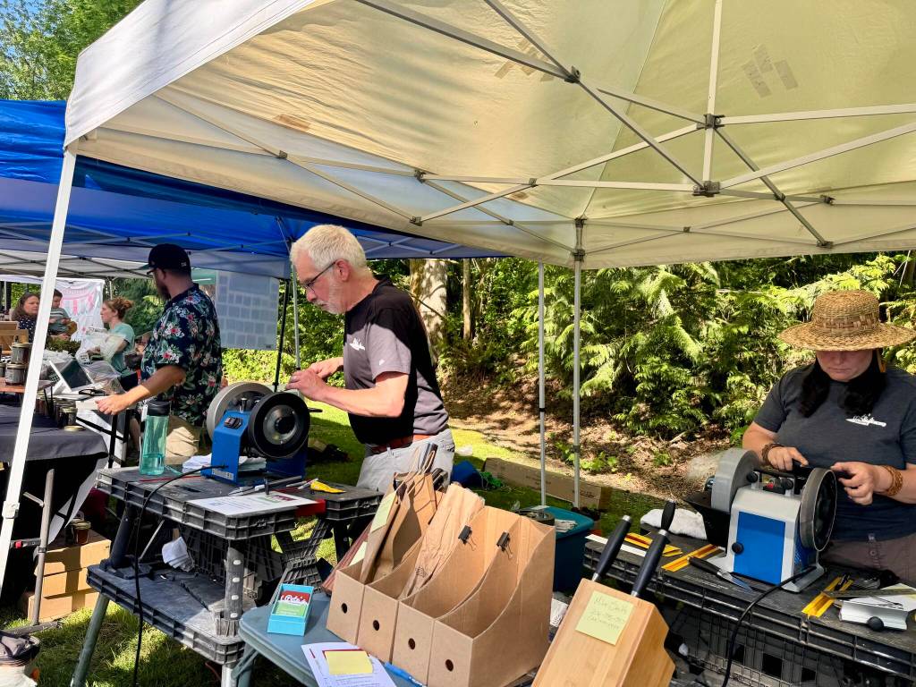 Local woodworker Pete Gillis (left) and his new apprentice, Erin Cox, sharpen knives at the Petes Sharpening booth at the Duvall Farmers Market, May 1, 2025.