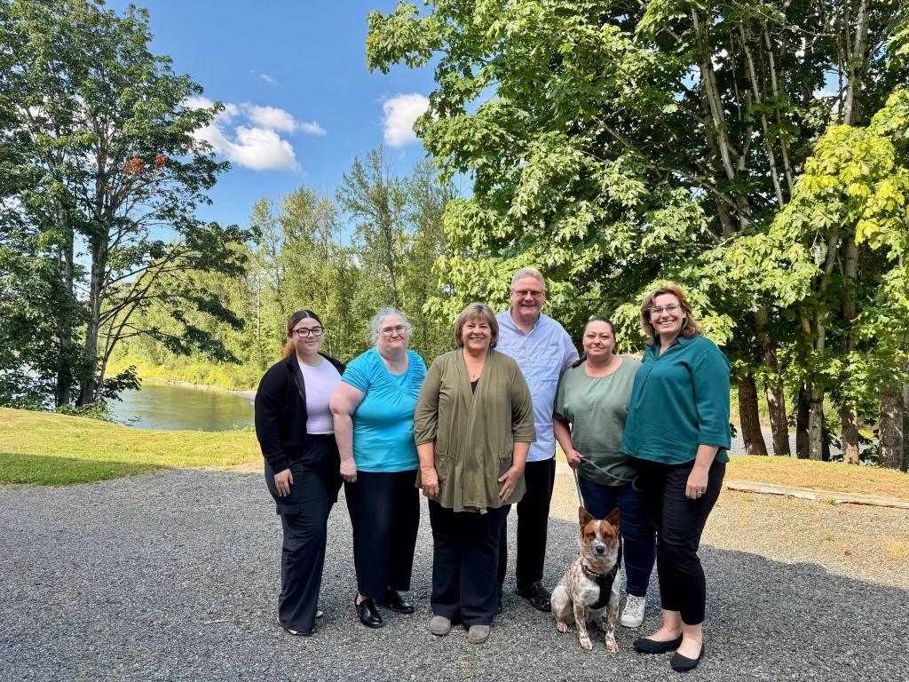 The staff of Hauglie Insurance, along with Copper the office dog, stands for a photo outside the agency by the Snoqualmie River, July 3, 2025. From left: Sophia Amaya Cruz, Elizabeth Gildersleeve, Laurie Hauglie, Kevin Hauglie, Samantha Darnell, Angela Donaldson. Grace Gorenflo/Valley Record