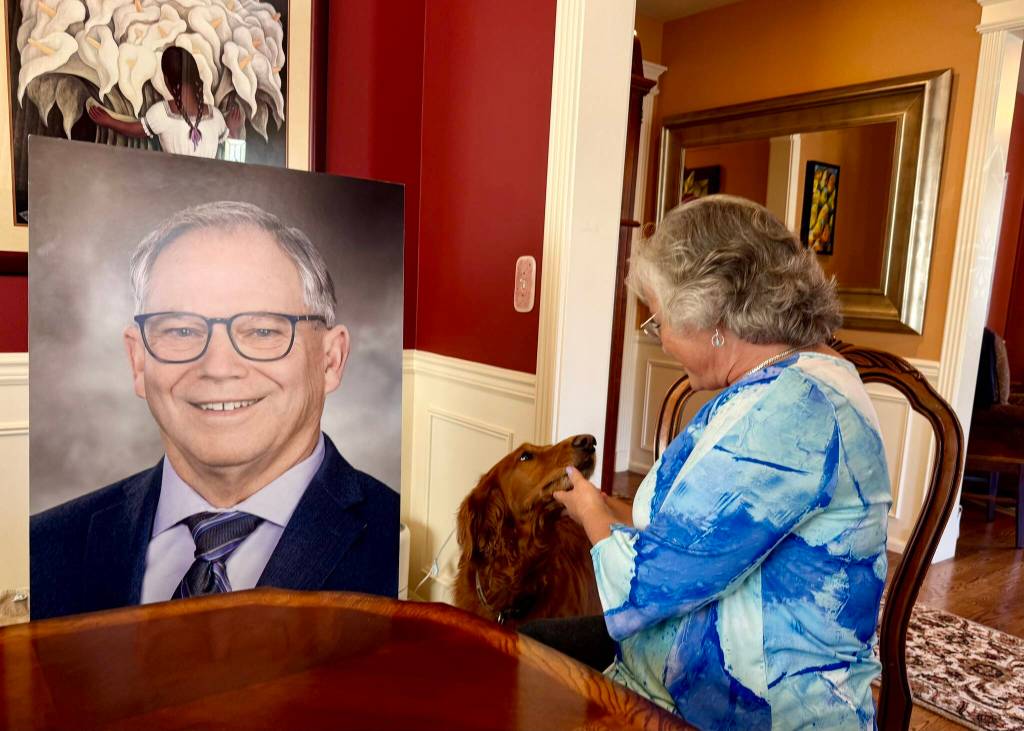 In her Issaquah home, Sarah Perry and her dog, Sadie, sit with the photo of Bill Ramos used for his celebration of life, July 30, 2025. Perry said she keeps the photo in her home office so Ramos is always with her. (Grace Gorenflo/Valley Record)