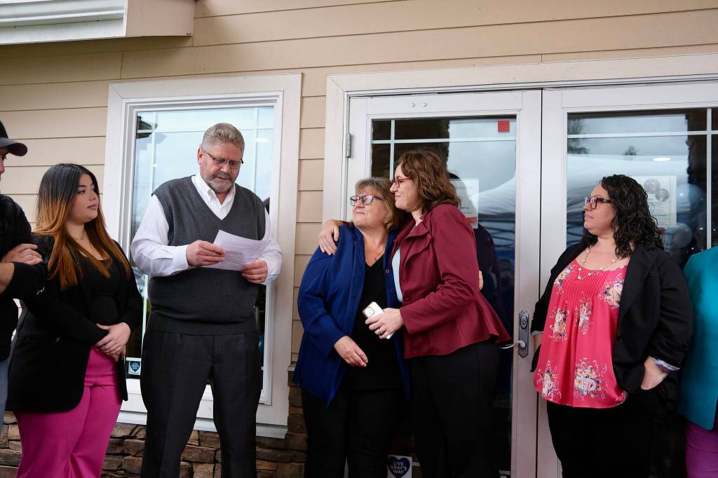 Angela Donaldson (center right) hugs her mom, Laurie Hauglie, as her dad, Kevin Hauglie, reads a speech, March 24, 2026. The Hauglies have sold their insurance business to Donaldson after 40 years.