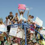 Local children hold protest signs on the playground at Fisher Creek Park, April 26, 2026.