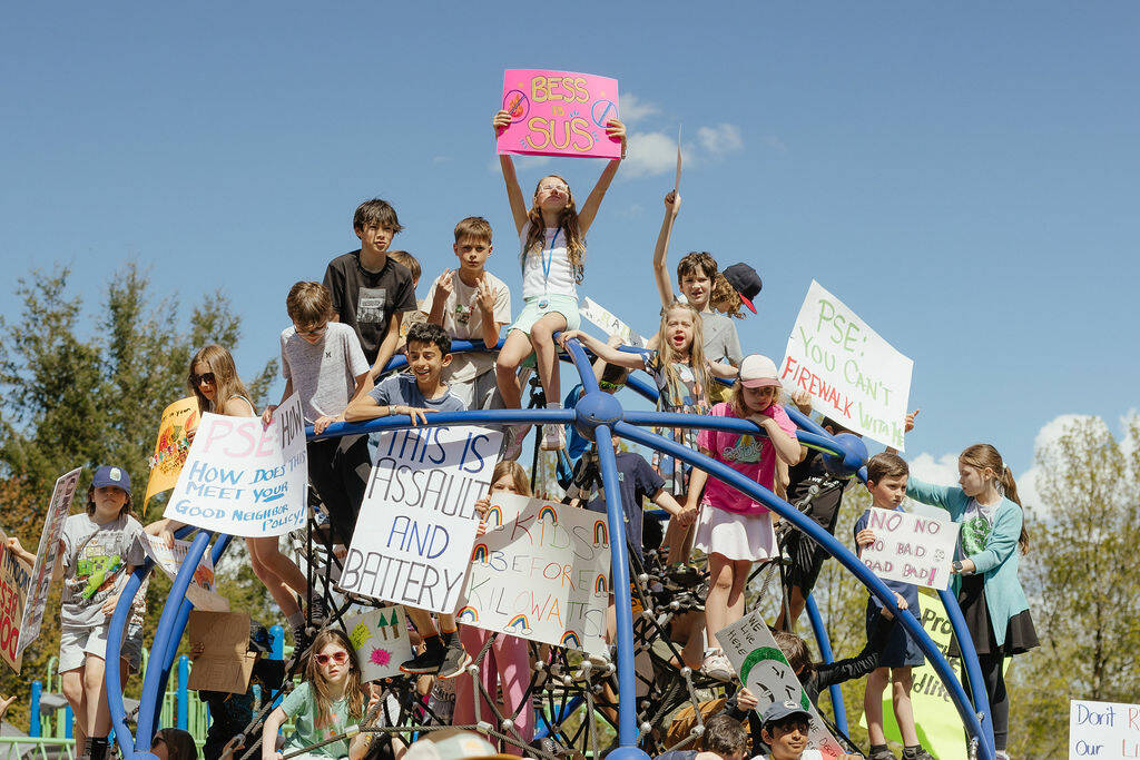 Local children hold protest signs on the playground at Fisher Creek Park, April 26, 2026.