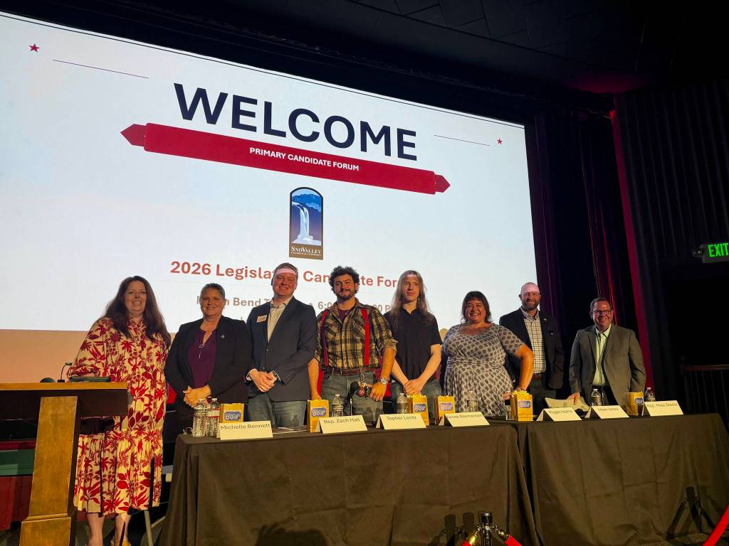 SnoValley Chamber of Commerce CEO Kelly Coughlin Games stands with candidates at a forum hosted by the chamber July 14, 2026. From left: Coughlin Games; Michelle Bennett; Zach Hall; Topher Leritz; Aimee Warmerdam; Maggie Adams; Adam James; Mike Steele. (Grace Gorenflo/Valley Record)